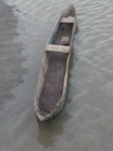 Une pirogue en bois abandonnée, échouée sur le rivage, avec des vagues douces et un ciel dégagé en arrière-plan.