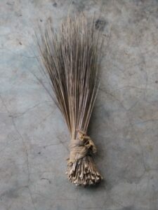 Image d'un balai africain artisanal utilisé pour balayer ou nettoyer une surface, fabriqué à partir de matériaux naturels.