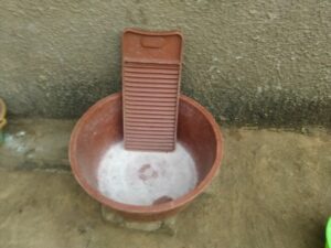 Image d'une planche artisanale en caoutchouc placée dans une grande bassine en plastique, utilisée pour laver les vêtements à la main dans un village africain.