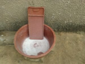Bassine en plastique accompagnée d'une planche en caoutchouc, utilisée pour laver des vêtements à la main.