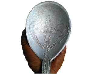 Une grande cuillère en bois ou en métal ornée de motifs de forgeron, utilisée pour remuer les sauces dans de grandes marmites traditionnelles africaines.