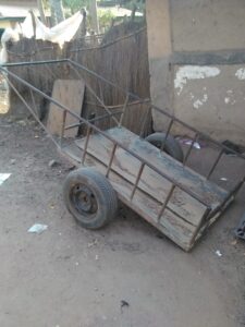 Un chariot traditionnel à deux roues, utilisé par des artisans ou des marchands africains pour transporter des marchandises ou des objets lourds dans un environnement rural ou urbain.