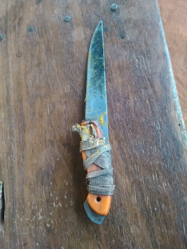 Un couteau africain traditionnel, fabriqué à la main avec une lame en métal et un manche en bois sculpté, posé sur une surface en bois.