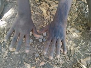 Les mains d’un enfant africain posées sur le sol, en train de manipuler des noix de palmier.