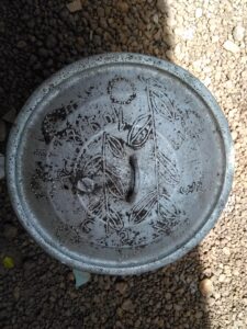 Couvercle en fer orné de motifs traditionnels, utilisé pour recouvrir une grande marmite dans la cuisine africaine.