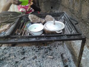Une petite fille devant un fourneau, apprenant à cuisiner avec de petites marmites sur un feu, une scène typique de l'apprentissage culinaire en Afrique.