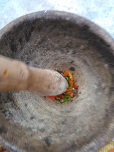 "Mortier en bois avec de petits piments rouges et un pilon, prêts à être écrasés."