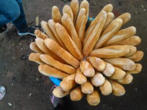 Des pains fraîchement cuits disposés dans une grande bassine, sortis d'un four africain traditionnel, prêts à être vendus dans un marché local.