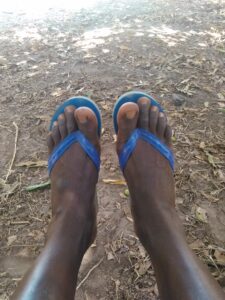 Un homme assis sous un grand arbre, les pieds étendus, dans un paysage calme et sauvage de l'Afrique. L'ombre de l'arbre apporte une sensation de fraîcheur et de tranquillité.