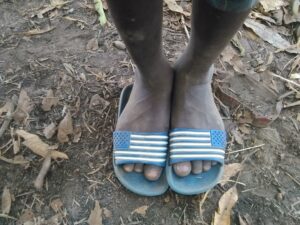 Les pieds d’un enfant posés sur un repose-pieds, avec un sol africain en arrière-plan.