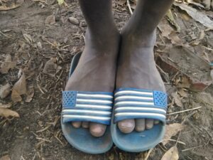 Pieds d’un enfant reposant sur un repose-pieds, avec un sol africain visible en arrière-plan.