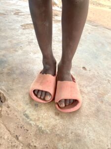 Pieds d'un enfant posés sur un repose-pieds, avec un sol africain visible en arrière-plan.