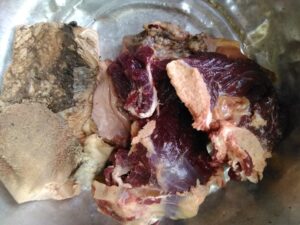 Panier rempli de viande de mouton fraîchement découpée, avec des épices et des légumes, typique d'un marché en Afrique.