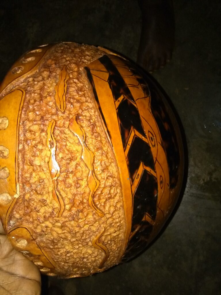 Une calebasse traditionnelle africaine posée au sol, ornée de motifs décoratifs, représentant l'artisanat local.