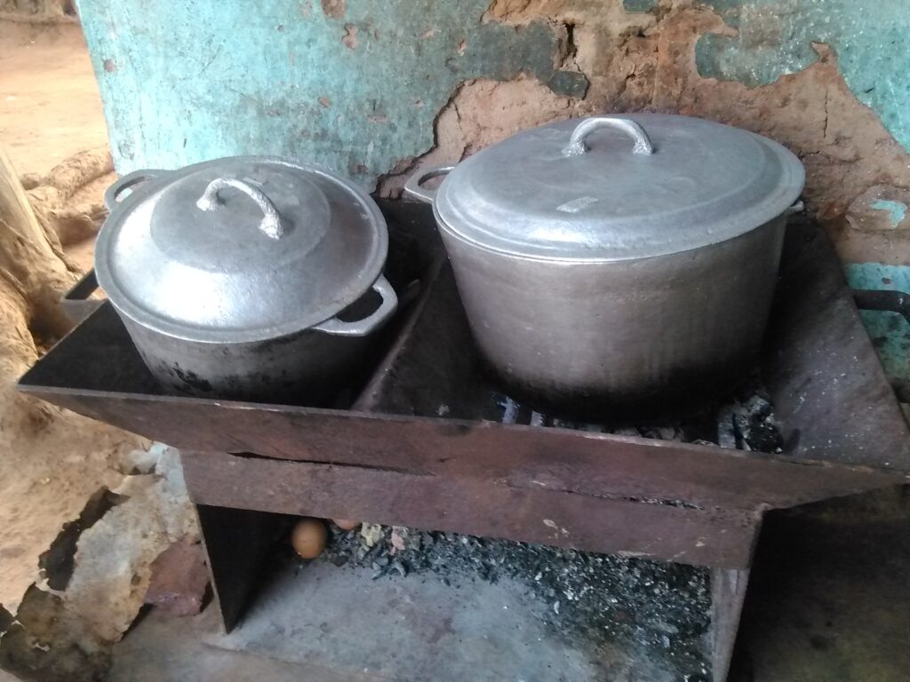 Grande marmite ouverte sur un fourneau de charbon ardent, préparation de repas familial en Afrique.