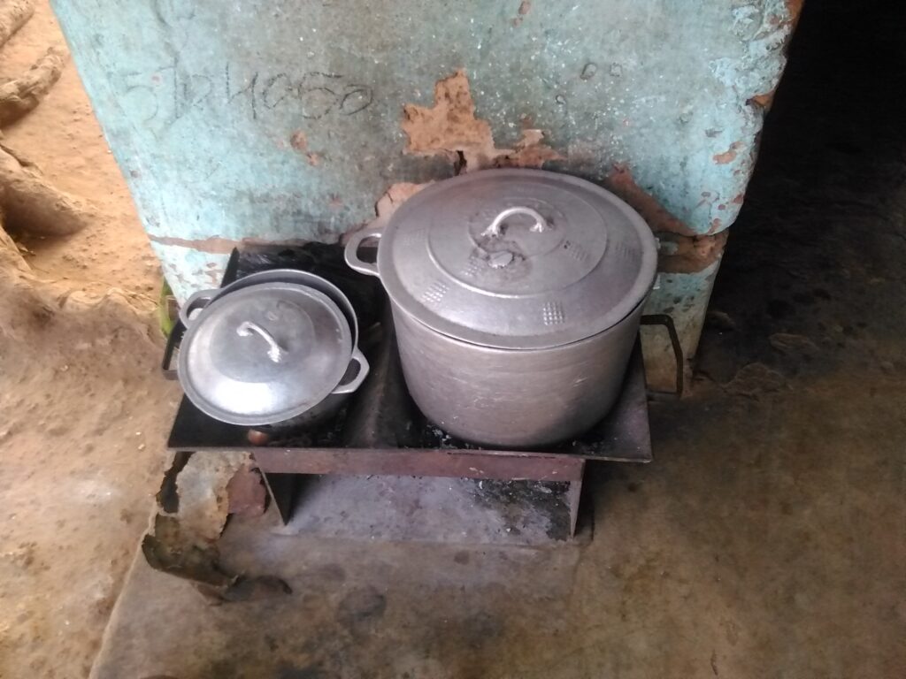Grande marmite ouverte chauffée par un fourneau de charbon, scène de cuisson familiale en Afrique.