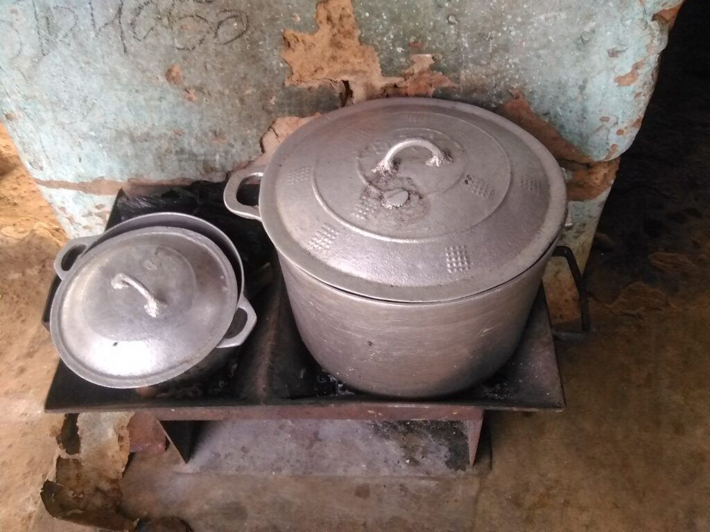 Grande marmite ouverte sur un fourneau de charbon en feu, scène de préparation de repas familial en Afrique.