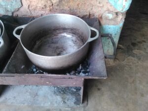Une marmite mijote sur un fourneau traditionnel alimenté par du charbon ardent.