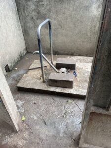 Installation simple de forage d'eau avec pompe et seaux, dans un décor de village africain.