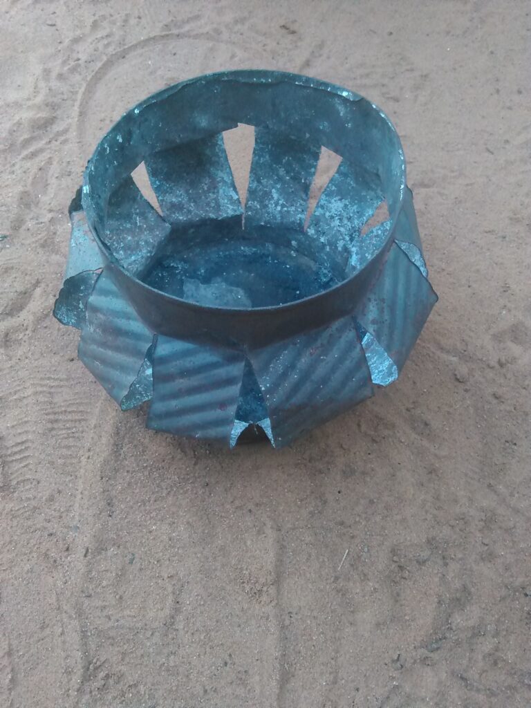 Photo d’un petit réchaud africain utilisé pour faire chauffer de l’eau, avec une tasse de thé à proximité.