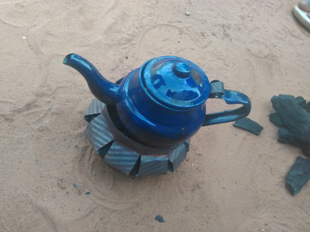 Image d'un petit fourneau ou réchaud traditionnel utilisé en Afrique pour préparer le thé, avec une tasse à thé posée à côté.