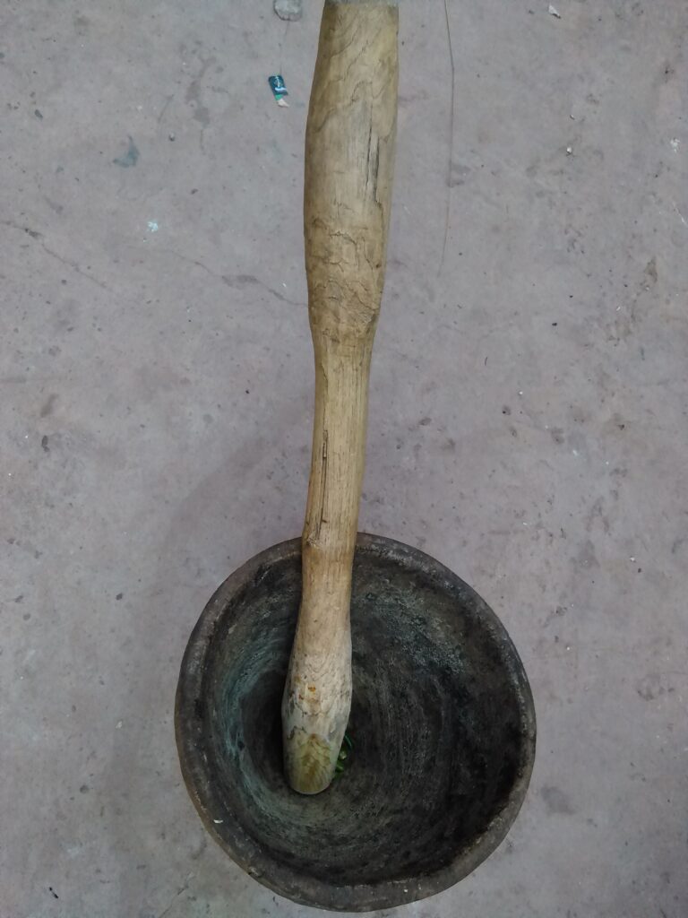 Un petit mortier et pilon en bois, traditionnellement utilisé pour moudre des épices africaines, posé sur une surface en bois.