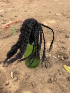 Poupée artisanale en bouteille avec des cheveux afro-texturés, portant des vêtements traditionnels africains.