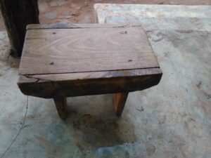 Un petit tabouret en bois, simple et rustique, rappelant le mobilier traditionnel des villages.